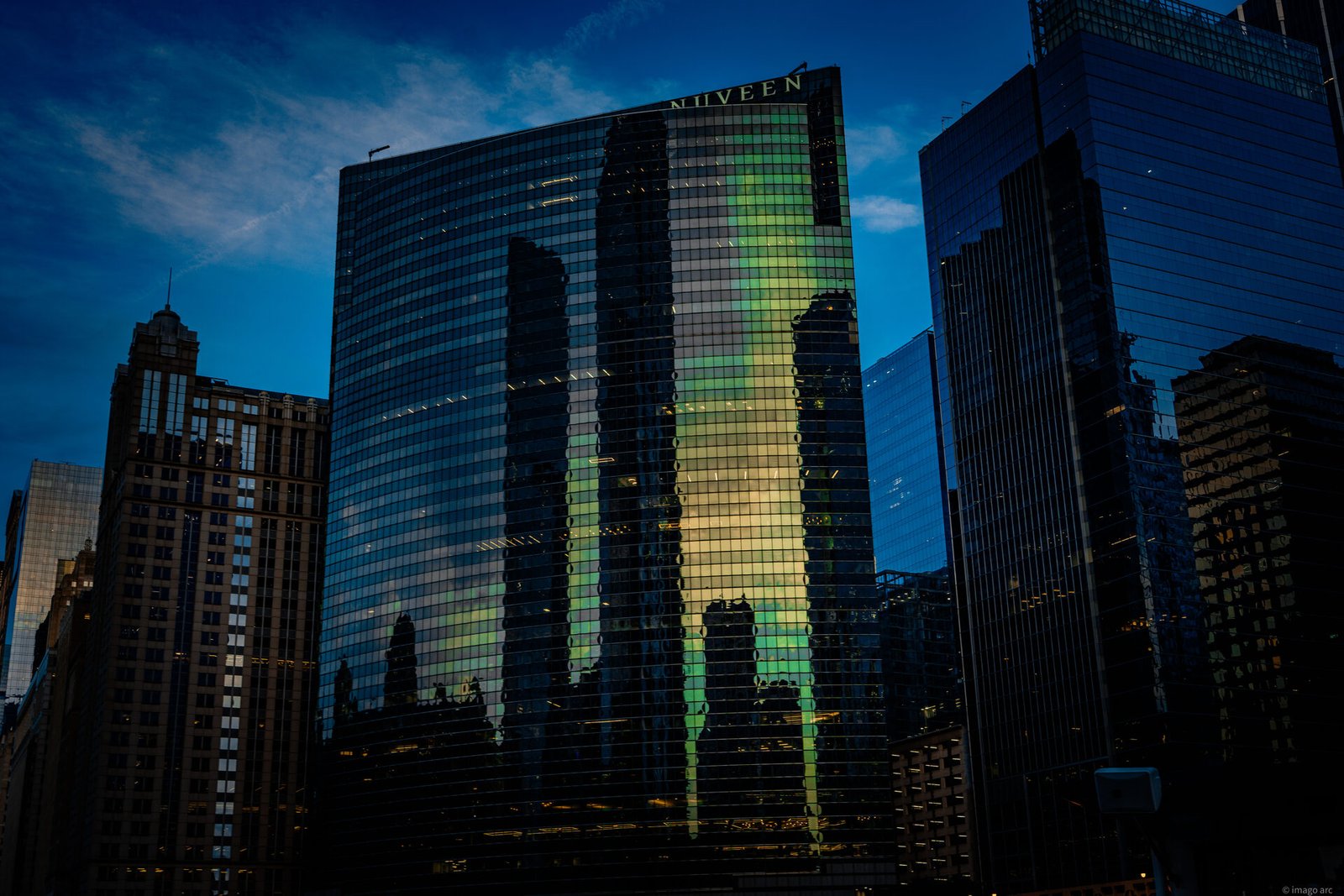Chicago skyscraper at dusk, city buildings reflected in a green-tinted glass curtain wall