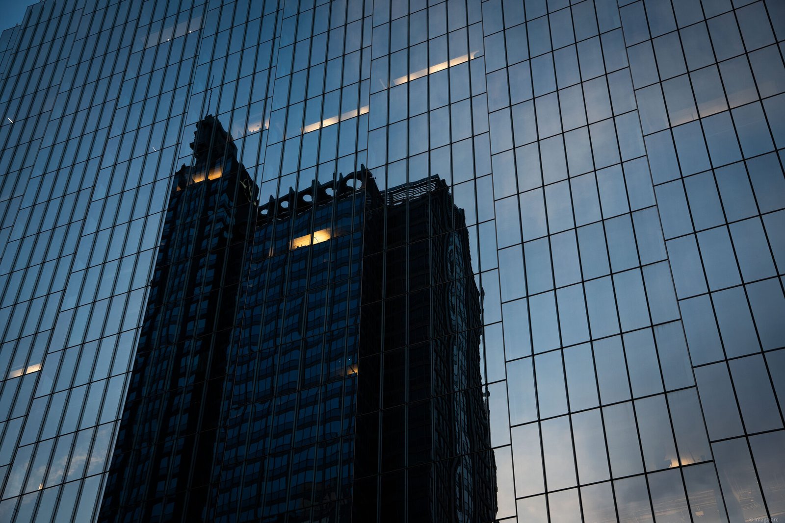 Older Chicago building reflected in the glass facade of a modern tower at dusk, abstract blue tones